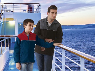 Dois rapazes no convés de um navio com casacos de inverno e mar ao fundo ao pôr do sol