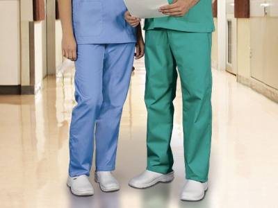 Duas pessoas com calças azul claro e verde e sapatos brancos em corredor hospitalar