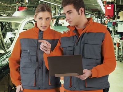 Duas pessoas com coletes de trabalho cinzentos e laranja numa fábrica automóvel