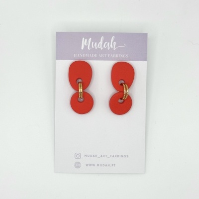 Brincos artesanais vermelhos com formas geométricas e argolas douradas em cartão de exposição