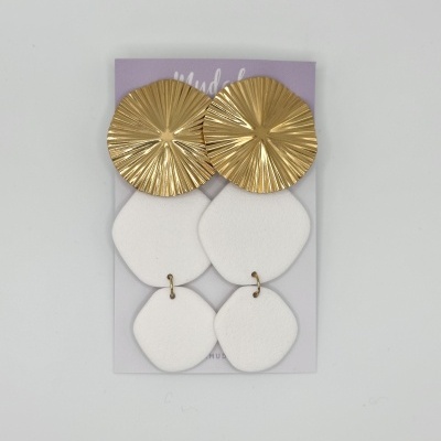 Brincos em peças douradas e brancas sobre cartão lilás