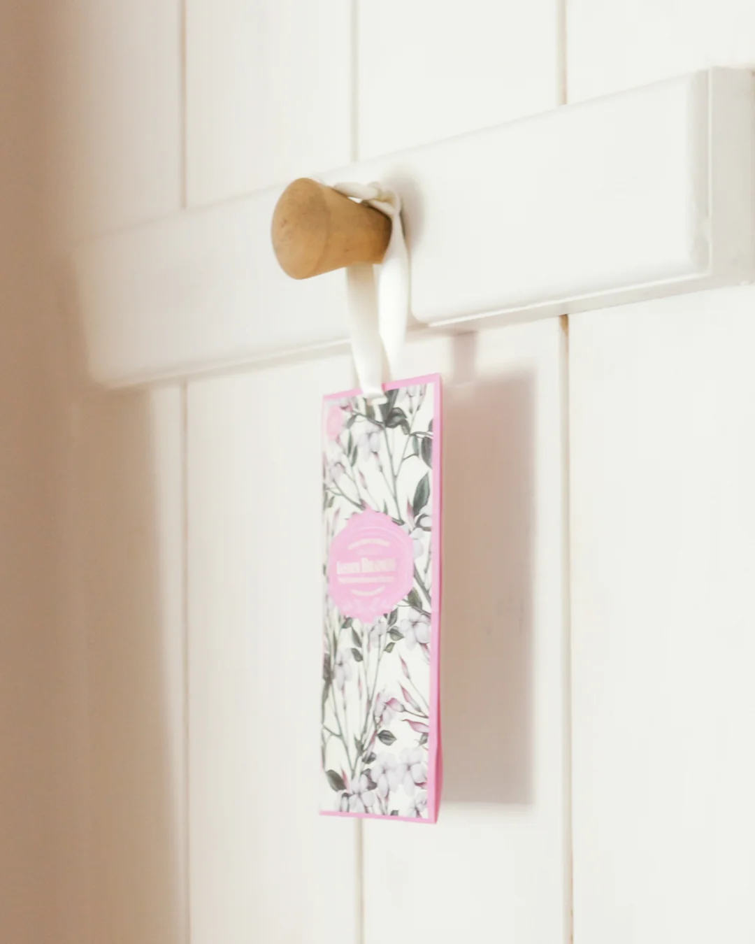 Sachete aromático floral pendurado em porta branca de madeira com puxador de madeira clara