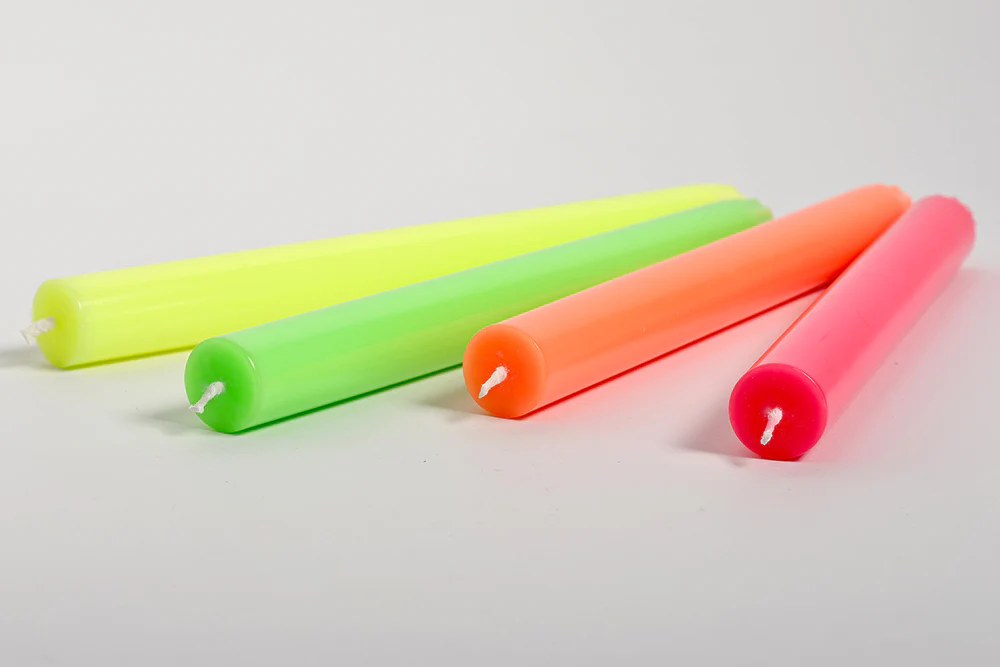 Quatro velas cilíndricas neon em amarelo, verde, laranja e rosa com pavios brancos