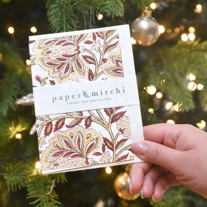 Cartão floral paper mirchi com texto em faixa branca junto a árvore de Natal