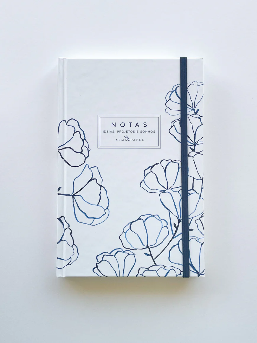 Caderno branco com desenhos florais azuis e texto central com elástico azul.