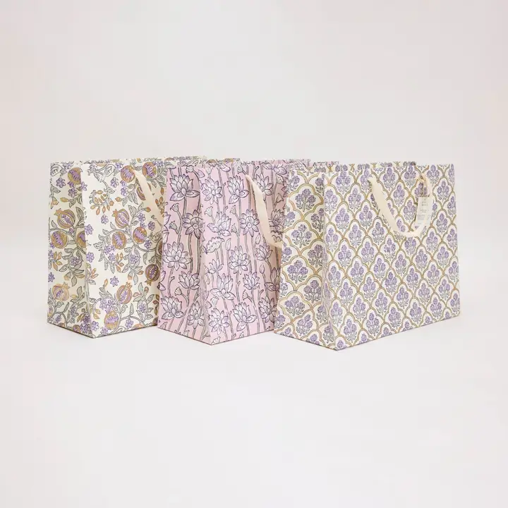 Três sacos de presente em papel com padrões florais e alças de fita