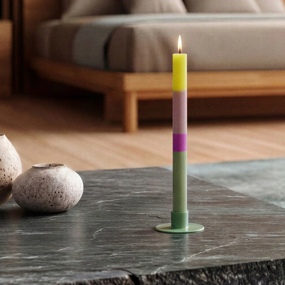 Vela de cera multicolor em castiçal verde numa mesa de pedra escura