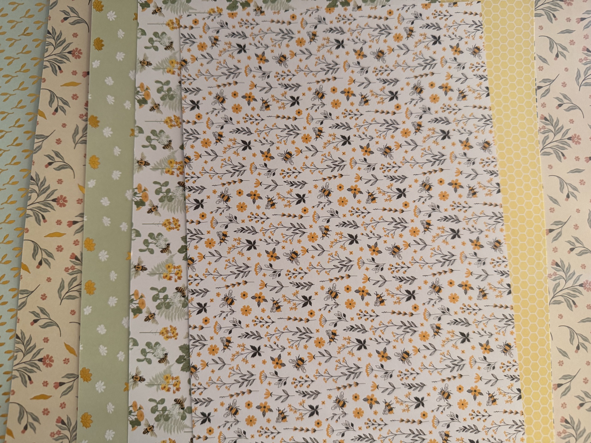 Folhas de papel decorativas com padrões florais e abelhas em tons amarelo, verde e bege
