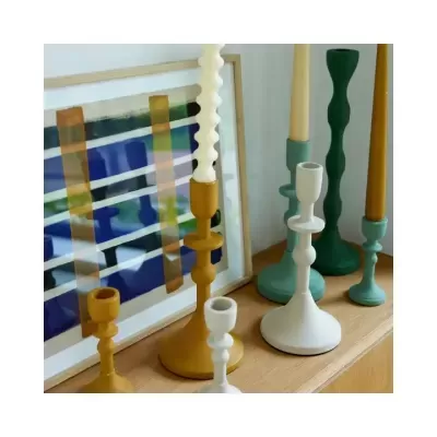 Castiçais metálicos coloridos com velas sobre móvel de madeira junto a quadro abstrato.