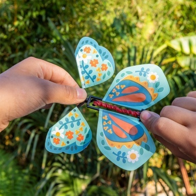 Brinquedo de borboleta em papel colorido com padrão floral, segurado por mãos ao ar livre