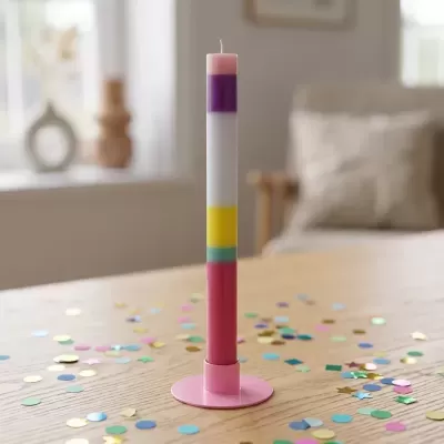 Vela alta colorida em suporte rosa sobre mesa de madeira com confetes coloridos