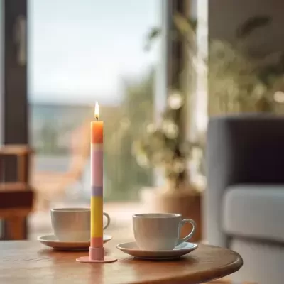 Vela colorida com suporte rosa e chávenas brancas numa mesa de madeira