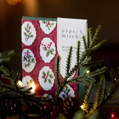 Livro com capa vermelha com estampado de azevinho e raminhos verdes com luzes