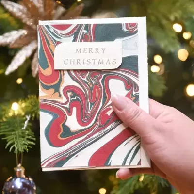 Cartão de Natal com padrão marmoreado vermelho, verde e dourado com texto MERRY CHRISTMAS