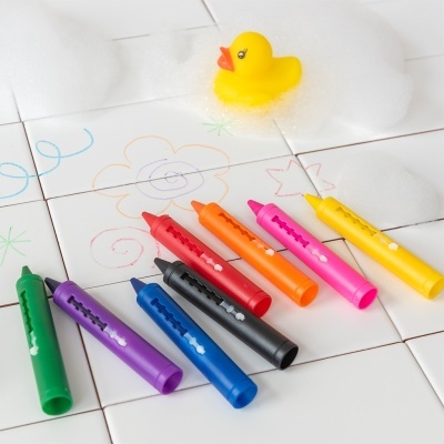 Lápis de cera coloridos sobre azulejos com desenhos e patinho de borracha amarelo com espuma