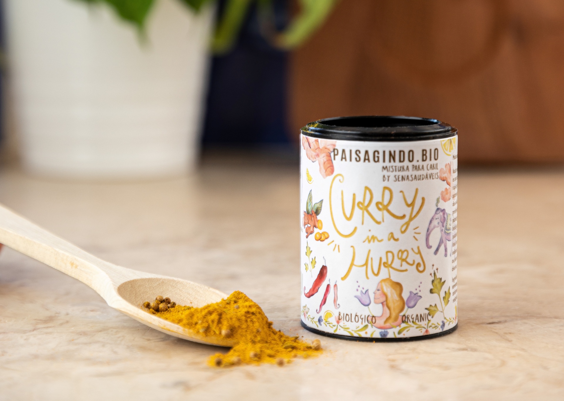 Curry in a Hurry by Senasaudáveis Lata de especiarias para caril biológica com colher de pau e pó amarelo sobre uma superfície clara.