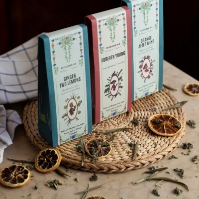 Três caixas de chá com design floral e textos distintos, sobre base de palha com fatias secas de limão em fundo de mármore.