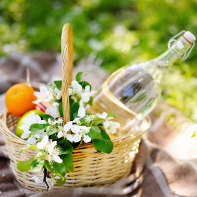 Cesto de verga com flores, garrafa de vidro, laranja e pano xadrez