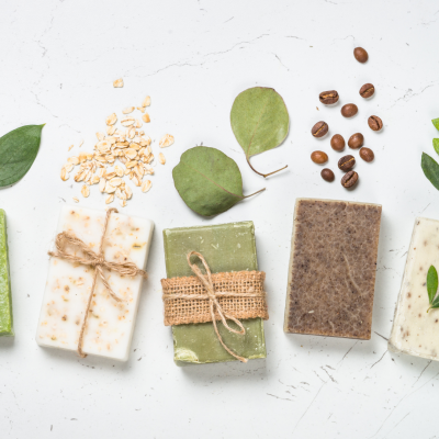 Sabonetes artesanais coloridos com folhas, aveia e café sobre fundo branco