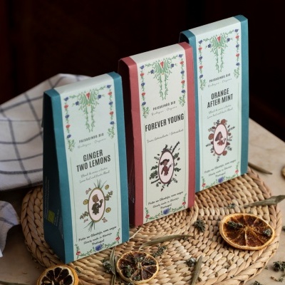 Embalagens de chá com design floral e textos variados sobre base de palha com fatias secas de laranja