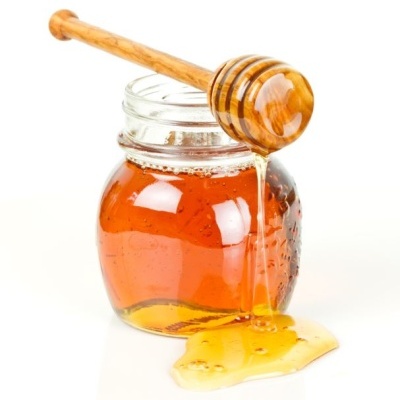 Frasco de vidro com mel dourado e colher de mel de madeira escorrendo mel.