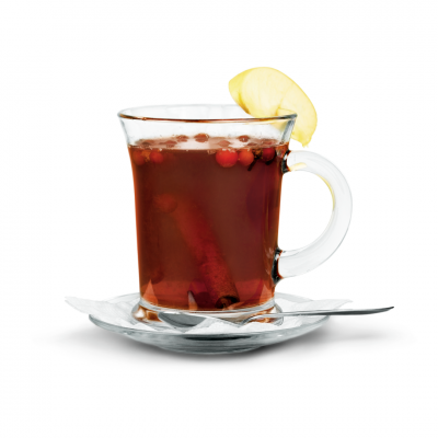 Copo transparente com chá quente, rodela de maçã, paus de canela e bagas vermelhas num prato transparente com colher e guardanapo