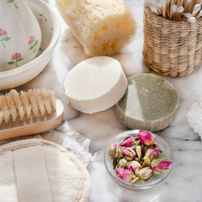 Produtos de higiene pessoal sobre superfície de mármore com barras de sabão, esponja natural e cesto de cotonetes