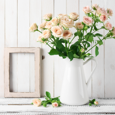 Vaso branco com flores cor-de-rosa sobre mesa rendada e moldura de madeira branca