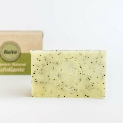 Sabonete exfoliante em barra bege com partículas pretas com embalagem ao fundo