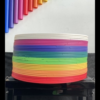 Discos coloridos empilhados numa mesa preta com tubos coloridos na parede atrás.