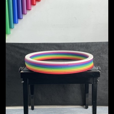 Círculo de plástico colorido com cores do arco-íris num banco preto e canetas coloridas na parede