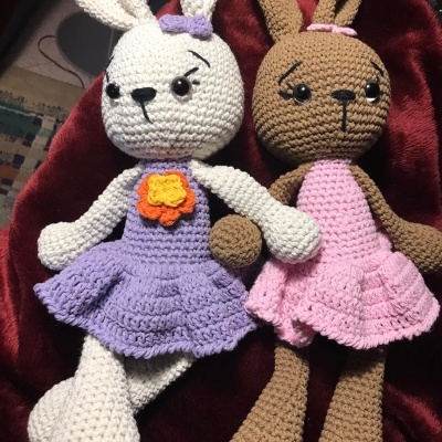 Dois coelhos de croché em saias coloridas deitados sobre tecido vermelho.