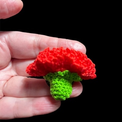 Flor vermelha de crochê com caule verde, em fundo preto, segurada por mão