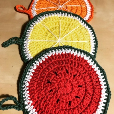 Descansos de panela em crochet em forma de fatias de frutas coloridas sobre uma superfície de madeira