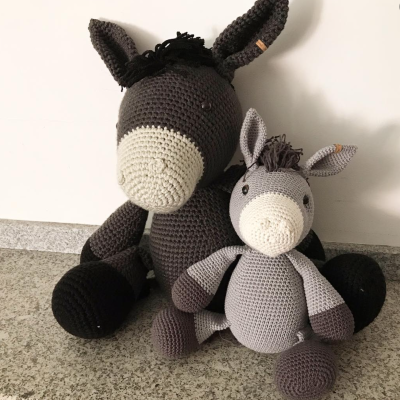 Dois bonecos amigurumi de burro em tons de cinza sentados lado a lado