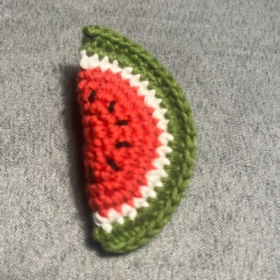 Fatias de melancia em crochet colorido sobre tecido cinza.