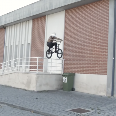 BMX a fazer salto junto a rampa de edifício com paredes de tijolos