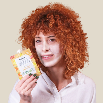 Pessoa com creme facial no rosto segurando embalagem amarela e branca de creme