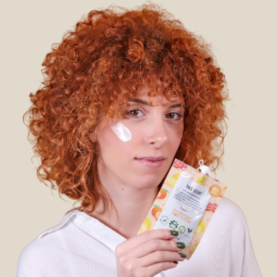 Mulher ruiva segurando embalagem de creme facial com frutas