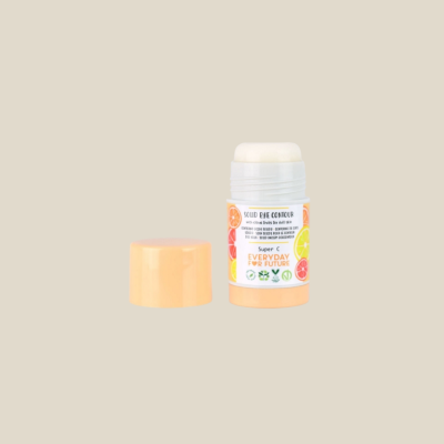 Bálsamo sólido para contorno de olhos em stick branco com tampa laranja claro e rótulo colorido com frutas cítricas.