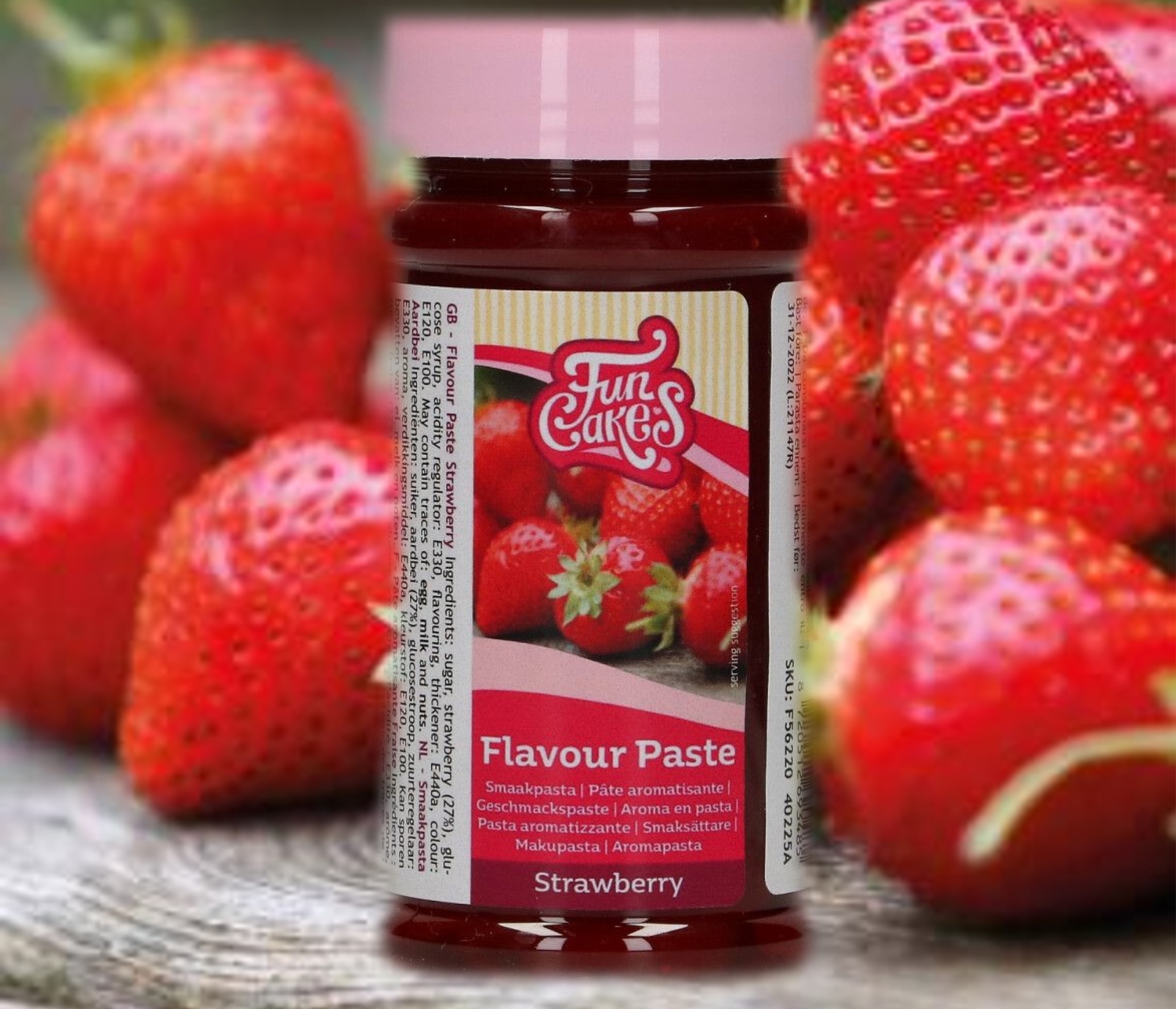 Frasco de pasta de sabor morango FunCakes com morangos frescos ao fundo
