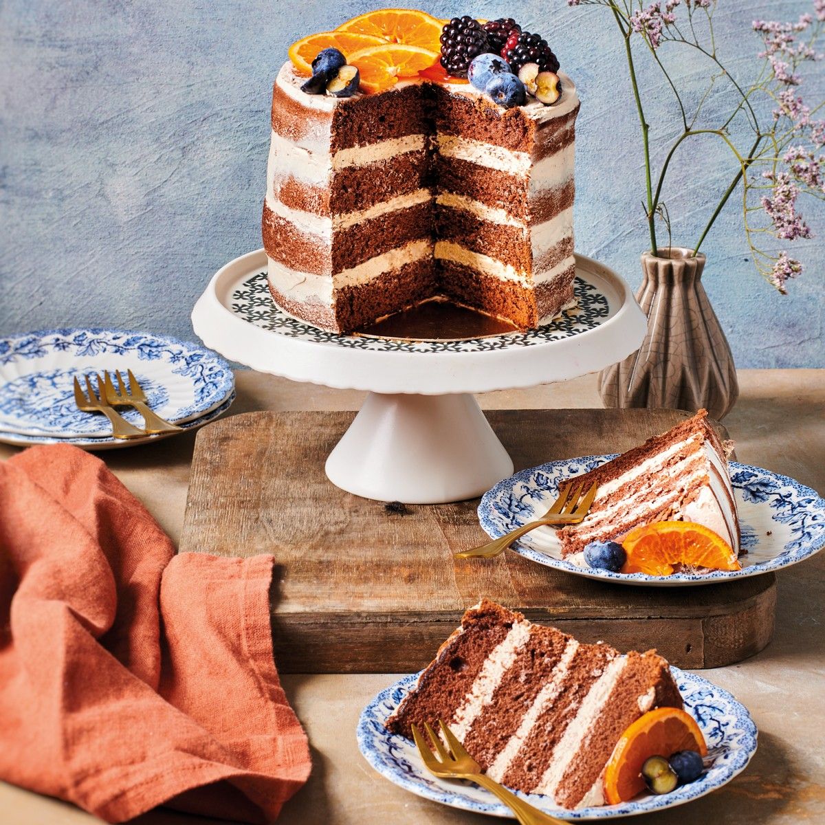 Mix Bolo Chocolate, 500gr Bolo de camadas com creme branco e chocolate decorado com fruta sobre prato branco e fatias em pratos azuis e brancos