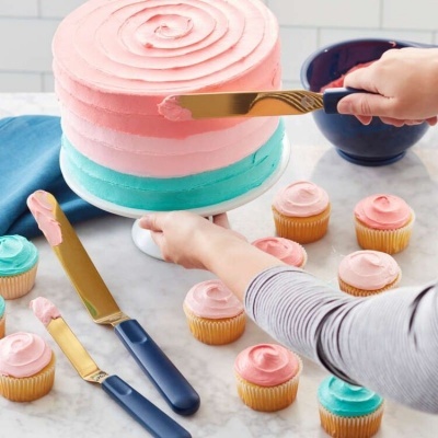 Bolo decorado com glacê rosa e azul acompanhado de cupcakes com glacê em cima de bancada de mármore