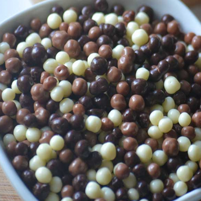 Bolas de chocolate brancas, castanho claro e castanho escuro numa tigela branca sobre madeira clara