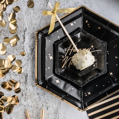 Prato preto decorado com estrelas douradas e texto 'Happy New Year' com bolo branco e confetes dourados