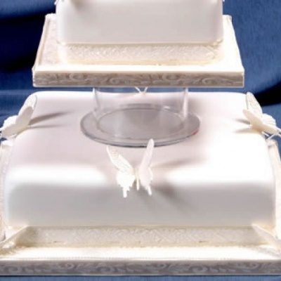 Bolo quadrado branco com borboletas e suporte transparente.