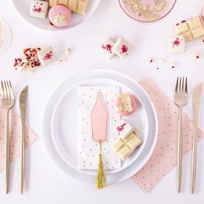 Mesa posta com pratos brancos, talheres dourados, guardanapos cor-de-rosa com pontos dourados e doces decorados em rosa, branco e dourado.