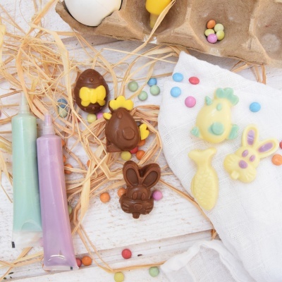 Doces de chocolate com formas de coelho, ovo e peixe, tubos de glacê, palha e pastilhas coloridas em fundo branco