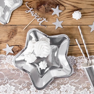 Mesa decorada com conjunto de festa prateado e branca com pratos estrela, copo metálico, canudos e decoração com estrelas e merengues.