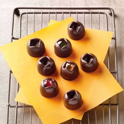 Bombons de chocolate com recheios coloridos em folhas amarelas sobre grelha metálica